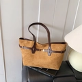 Brown suede tote bag with leather strap and gold buckle detail on a luxury black leather seat - Brown