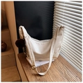 Detailed close-up of cream crescent shoulder bag with fuzzy brown pompom charm on wood table - White