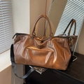 Large brown leather travel bag with adjustable strap and handles in a warm indoor setting - Brown
