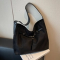 Bolso tote de ante negro con correas de cuero y ojales metálicos dorados sobre un libro - Negro