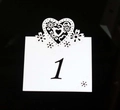 Close-up of laser-cut white wedding table card featuring intricate heart and flower lace detail - White
