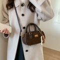 Donkerbruine suède Boston tas met kralenhanger en goudkleurige details op een beige jas - Bruin