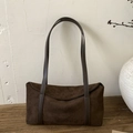 Detail of dark brown suede pillow bag with long leather strap on a rustic wooden surface - Brown
