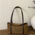 Detailed close-up of brown suede pillow bag on vintage wood with minimalist ceramic vase - Brown