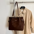 Detail einer dunkelbraunen Wildleder-Tragetasche mit Metallringen und Logo-Plakette - Braun