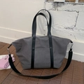 Détail d'un grand sac cabas en toile grise avec anses en cuir noir sur un sol en bois - Gris