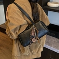 Retro black leather cylinder bag with donut charm shown in a stylish shoulder carry - Black with Pendant