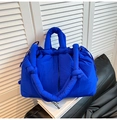 Dettaglio della borsa tote trapuntata blu reale con tracolla a nodi su un libro bianco - Blu