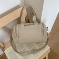 Große beige Reisetasche aus Nylon mit verstellbarem Gurt auf einem Holzstuhl - Cremeweiß