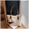 Detailansicht einer gewebten Tragetasche mit braunen Ledergriffen und einem Bärenanhänger - Beige Mit Anhänger