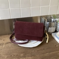 Burgundy faux suede crossbody bag with wood bead charm on a display plate - Red with Pendant