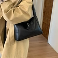 Minimalist large black tote bag with silver buckle worn by a model in a warm indoor setting - Black