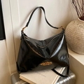 Bolso tote negro brillante retro con correa ancha y logo dorado sobre una maleta - Negro