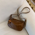 Bolso hobo de cuero marrón con colgante de cuentas de madera en un sofá beige - Marrón con colgante