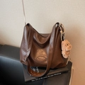 Dunkelbraune Retro-Tasche mit breitem Gurt und Plüschbär-Anhänger auf Ledersofa - Kaffeebraun (Mit Anhänger)