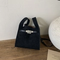 Detail view of black suede tote bag with silver metal twist lock and strap on wooden table - Black