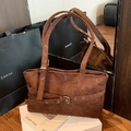 Dark brown suede tote bag with eyelet strap detail shown in a premium lifestyle setting - Brown
