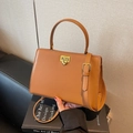 Minimalist brown leather satchel bag with gold buckle on a black book background - Brown