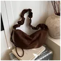 Detailed shot of dark brown suede hobo bag with unique ruffled strap design on a suitcase - Brown