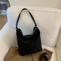 Detail view of black matte suede bucket bag with metal rivets on a white fabric sofa - Black