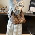 Leopard print crescent hobo bag with brown leather strap worn by a model in a cafe - Brown