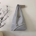 Minimalist light grey hobo bag with decorative belt and metal eyelets hanging on a wall - Gray
