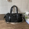 Detail einer großen schwarzen Ledertasche mit gewebtem Riemen auf einem Holztisch - Schwarz