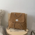 Close-up of brown suede backpack with quilted pattern and metal chain on wooden stool - Brown