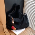 Retro black corduroy shoulder bag with colorful pompom charm on a sunny windowsill - Black