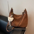 Braune Vintage Hobo-Tasche mit Leder- und Kettenriemen auf einem schwarzen Sofa - Braun mit Anhänger