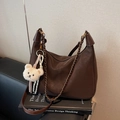 Dunkelbraune Hobo-Tasche aus Leder mit Kettenriemen und Bärenanhänger auf Buch - Kaffee mit Anhänger