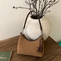 Detail view of brown suede baguette bag with leather strap and tassel on wooden surface - Brown