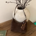Détail du sac hobo en daim marron foncé avec pompon bohème et perles sur surface en bois - Marron