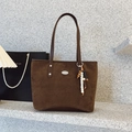 Bolso tote marrón de ante sintético con colgante de cuentas sobre fondo grisaceo - Marrón