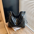 Bolso tote acolchado negro con correas de cadena dorada sobre banco madera - Negro
