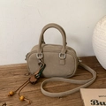 Dettaglio della mini borsa Boston kaki con ciondolo a nappa su superficie di legno - Con Ciondolo / Cachi