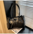 Dettaglio di borsa tote in pelle nera lucida con fibbia metallica su sfondo artistico - Nero