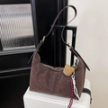 Dettaglio borsa hobo marrone scuro con ciondolo a orsetto su valigia bianca - Marrone