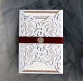Detail of laser-cut white invitation with red silk ribbon and sparkling crystal buckle - White