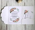 Detail of laser-cut floral wedding invitation with RSVP card on light wood background - White