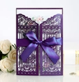 Macro detail of laser-cut purple wedding invitation with silk bow and floral insert - Deep purple