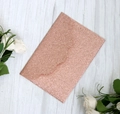 Sparkling rose gold glitter envelope with wavy flap on a white wood background - Apple Gold