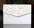 Dettaglio macro del motivo floreale bianco tagliato al laser su elegante invito - Bianco