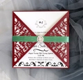 Detalle de invitación de boda bordeaux con corte láser, cinta de seda verde y hebilla de brillo - Rojo oscuro
