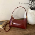 Dettaglio borsa sottobraccio in pelle rosso scuro con ciondolo d'oro su legno - Borgogna