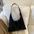 Detalle de un bolso hobo de ante negro con cremallera sobre un sofá blanco minimalista - Negro