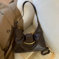 Deep brown crescent hobo bag with gold metal trim on a white soft sofa background - Brown