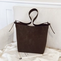 Dark brown matte leather bucket bag with adjustable thin shoulder strap on a white sofa - Brown