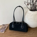 Detailed view of black suede baguette bag with contrast white stitching on a wooden surface - Black
