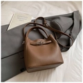 Chic brown lychee leather bucket bag with top handle and crossbody strap in neutral setting - Coffee without Pendant